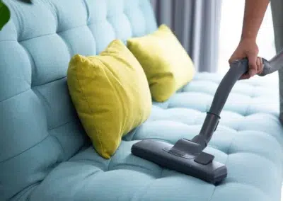 Personne passant l'aspirateur sur un canapé bleu avec coussins jaunes.